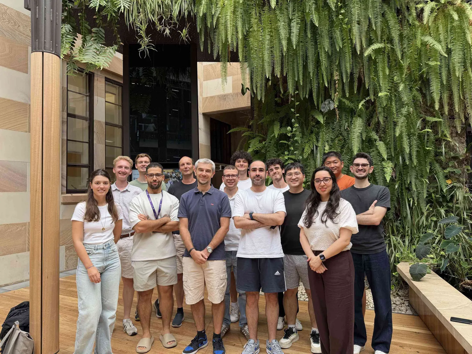 Large DLab group beside a green wall in a campus courtyard