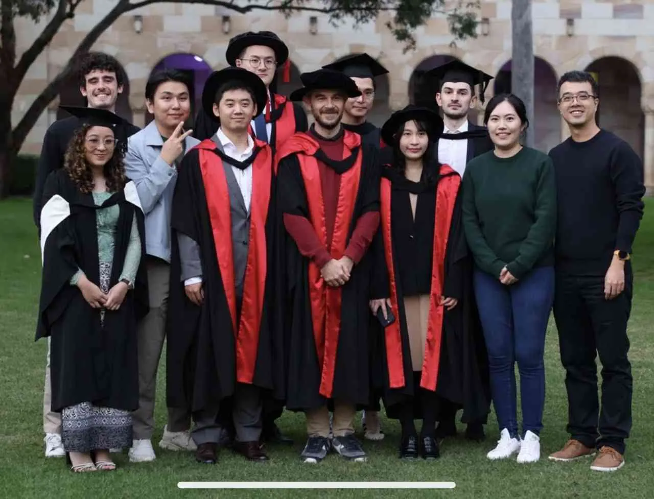 DLab members in graduation gowns with colleagues in the Great Court at The University of Queensland